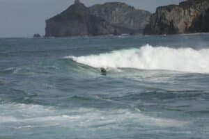 Surfer gracefully rides a wave near rugged cliffs under a clear sky, embodying a dynamic surfing adventure.
