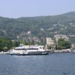 Boat cruising on Lake Como with lush hills and marina in the background.