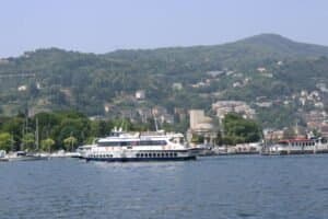 Boat cruising on Lake Como with lush hills and marina in the background.