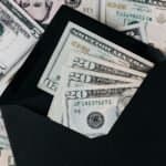 From above of dollar bills in opened black envelope placed on stack of United states cash money as concept of personal income