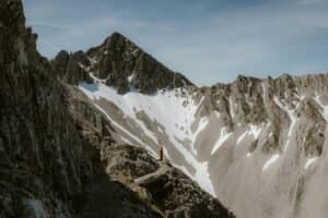 A lone hiker stands amidst a dramatic mountain landscape under a clear sky.