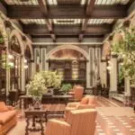 A luxurious hotel lobby featuring elegant architecture, rich decor, and comfortable seating under a stained glass ceiling.