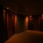 A dark, quiet hotel corridor featuring multiple closed wooden doors and soft lighting.