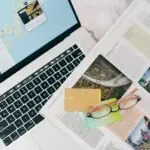 A top view of travel planning essentials on a laptop with a map, credit cards, and a magazine.