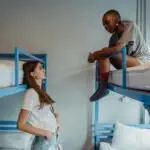 Two young women engaging in conversation in a casual hostel setting with blue bunk beds.