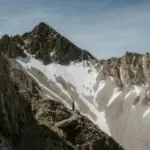 A lone hiker stands amidst a dramatic mountain landscape under a clear sky.