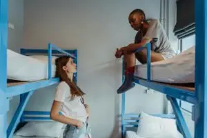 Two young women engaging in conversation in a casual hostel setting with blue bunk beds.